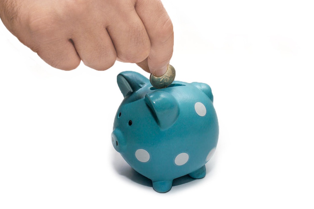 En hånd der putter en mønt i en turkis sparegris med hvide prikker, illustrerer opsparing og finansiel uddannelse.