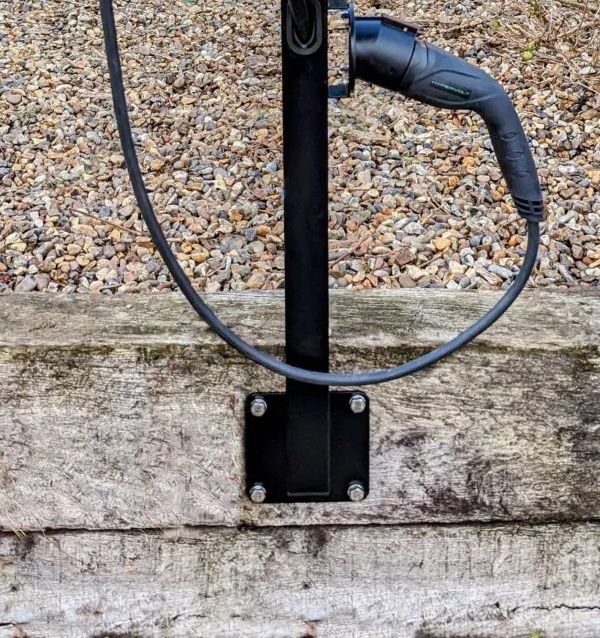 Et sort ladestik til elbil monteret på en stolpe ved en trævæg.